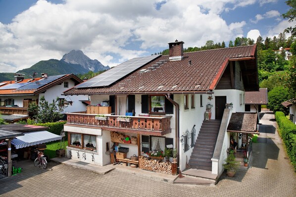 A two-story building with a balcony, solar panels, and a mountain in the background.
