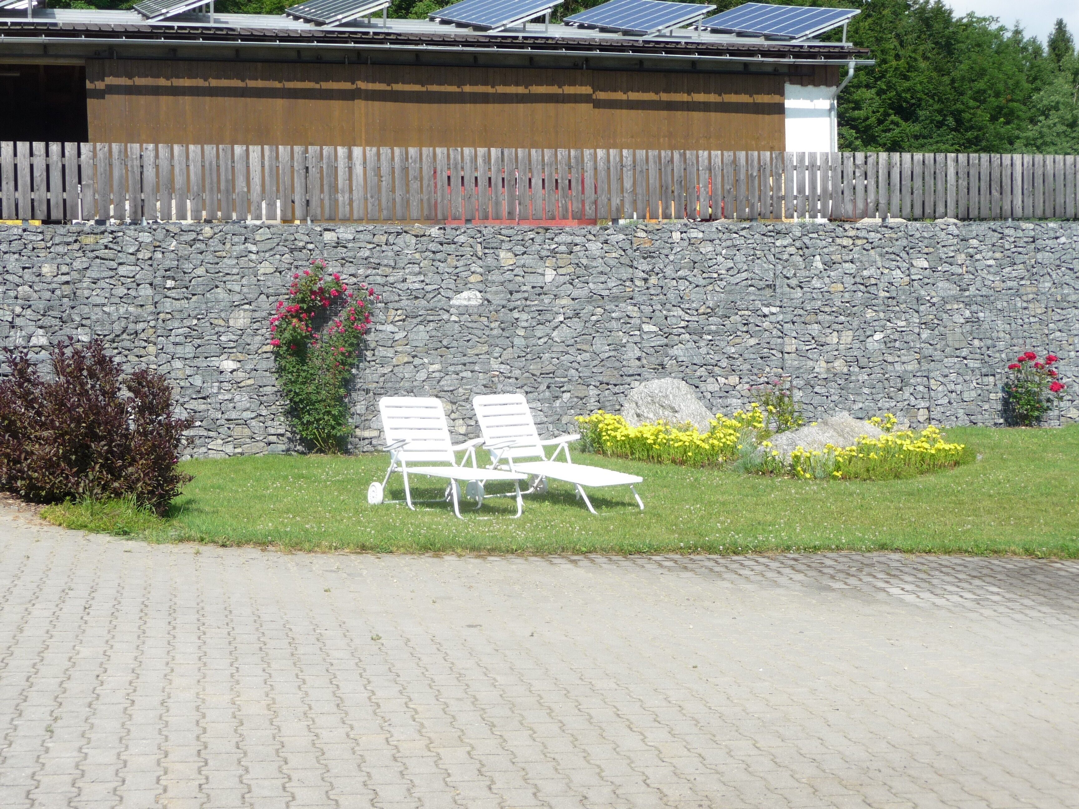 A stone wall, two white lounge chairs, and a paved walkway.