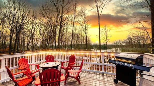 A deck with red Adirondack chairs, a grill, and a view of trees and sunset. - Lake - King - Gym - Kayak - Fire Pit - PetsOK - WD (Ashford)