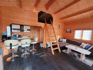 Een gezellig cabin interieur met een eethoek, een bank, een ladder en een keuken.