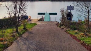 Un sendero que lleva a un lago con una estructura verde en el centro, rodeado de árboles y un cartel.