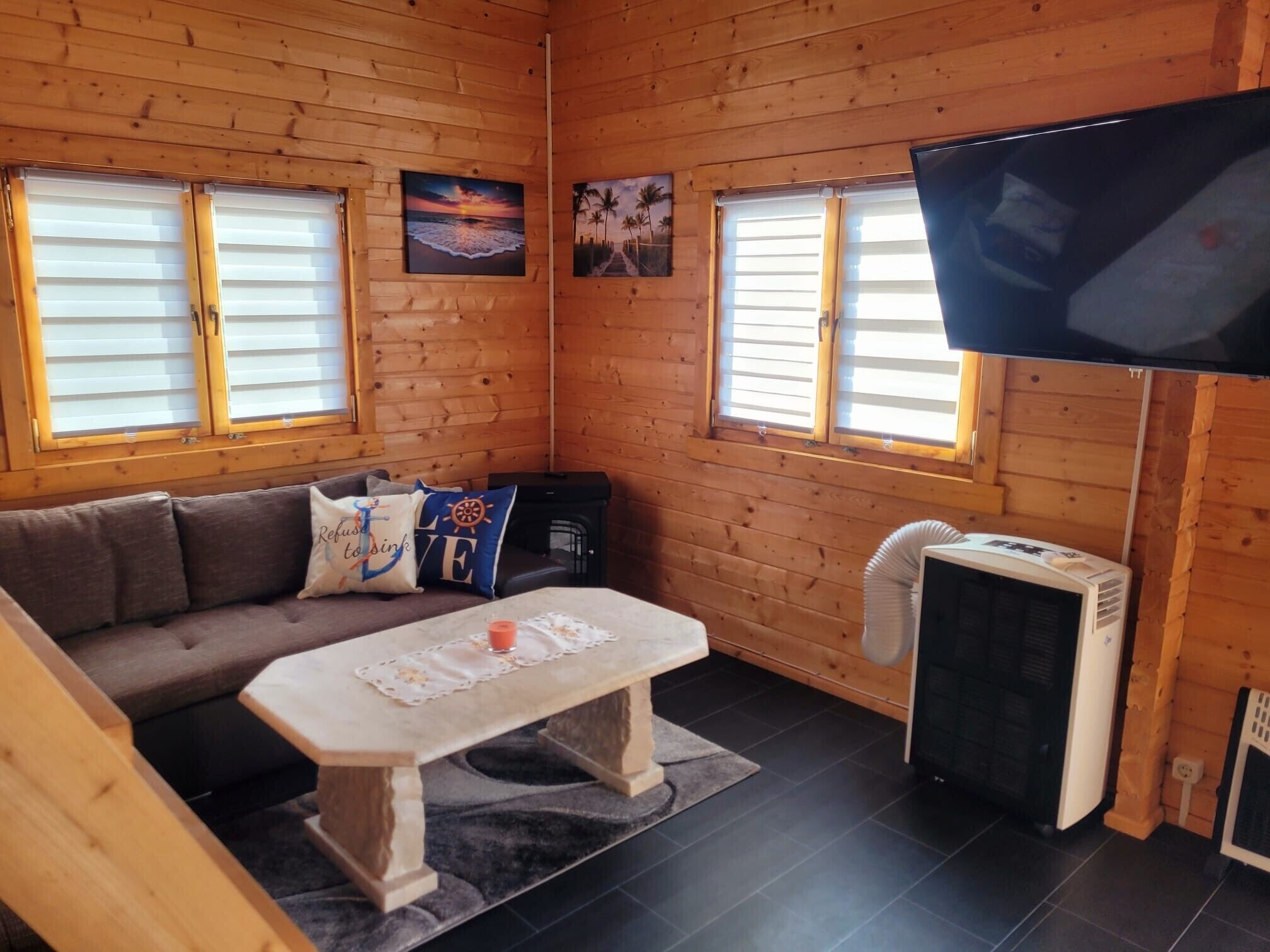 A cozy cabin interior with a sofa, a table, a TV, and two windows with blinds.