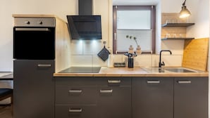 Una cocina moderna con horno empotrado, extractor de aire negro, ventana con persianas y encimera de madera.