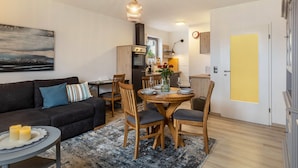 Una sala de estar moderna con sofá, mesa de comedor, sillas y una cocina al fondo.