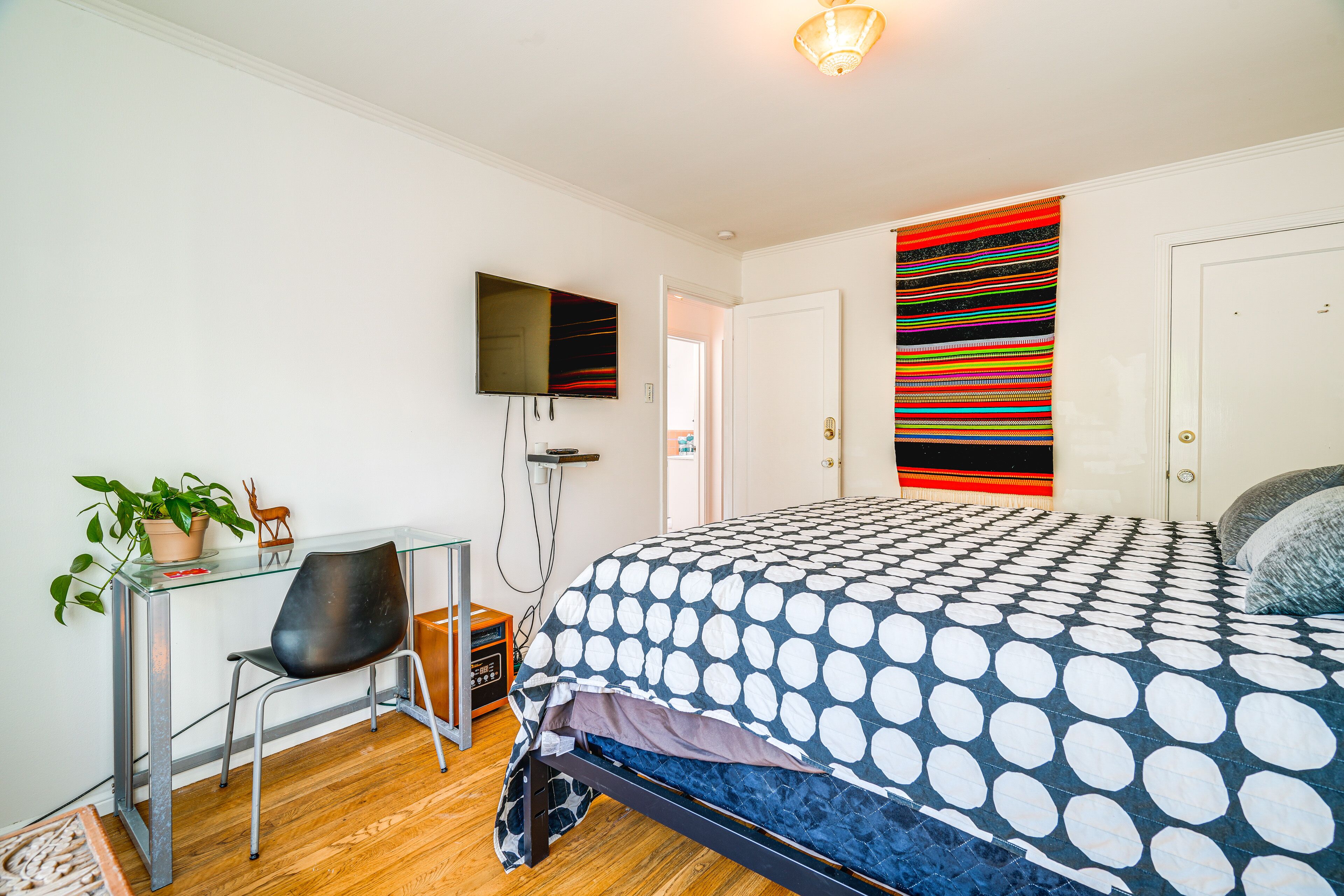 Een slaapkamer met een bed, een bureau met stoel, een televisie en een deur.