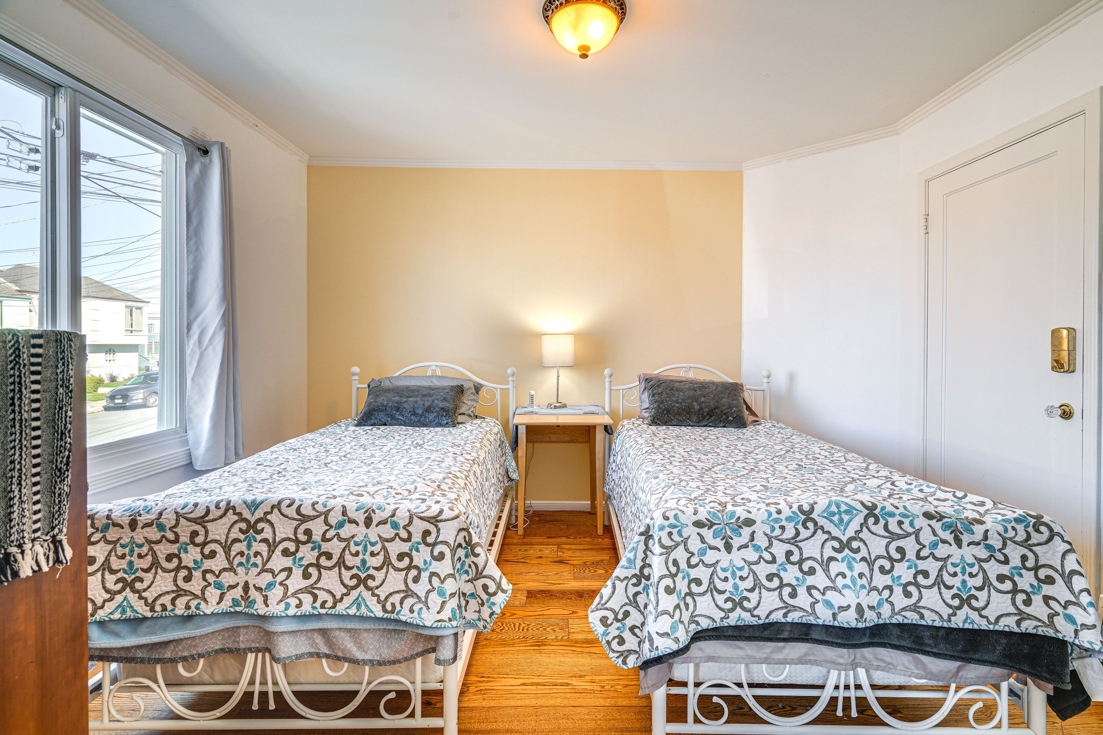 A room with two beds, a nightstand, a lamp, and a window with curtains.