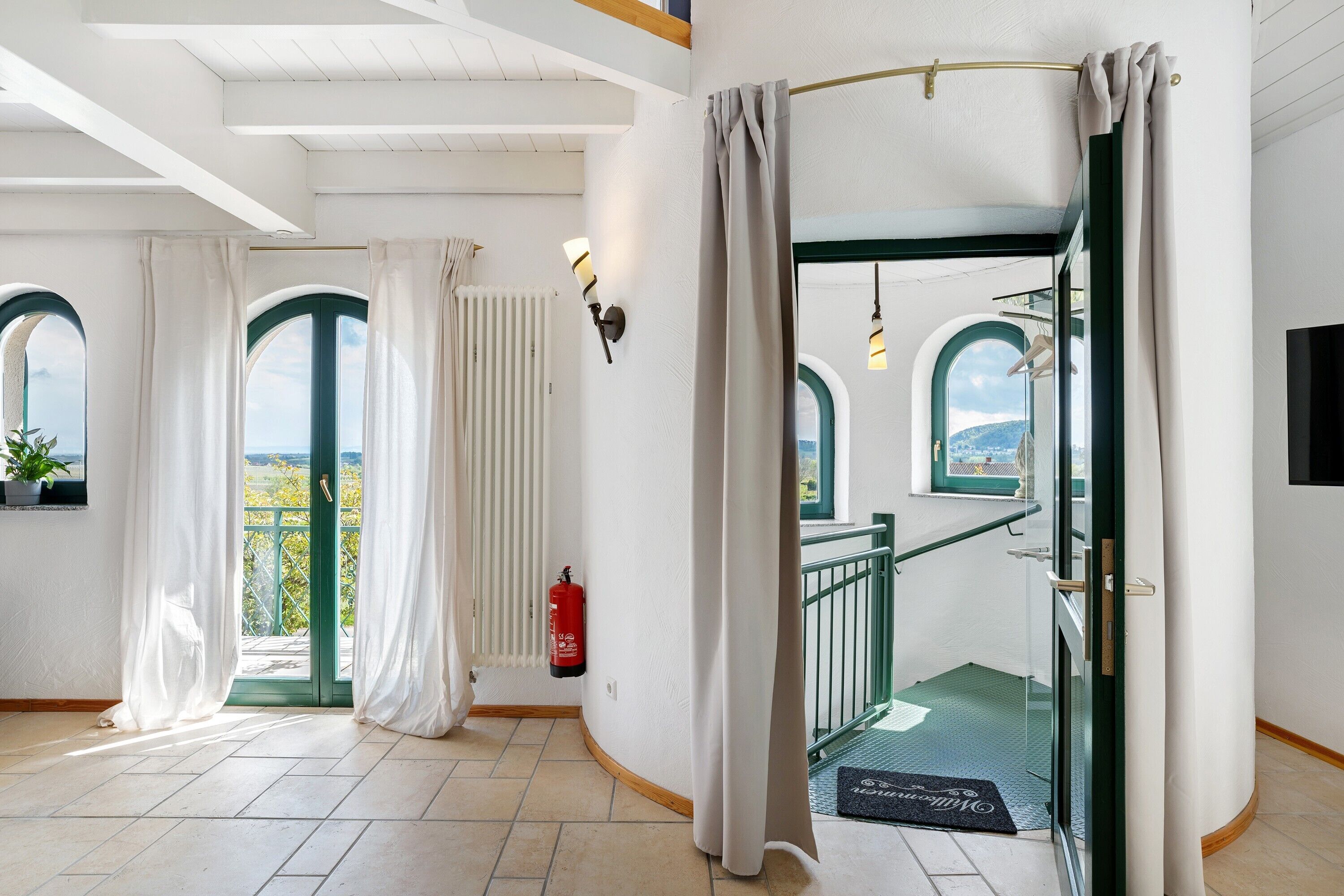 A hotel room with a view, a fire extinguisher, a door with curtains, and a staircase.