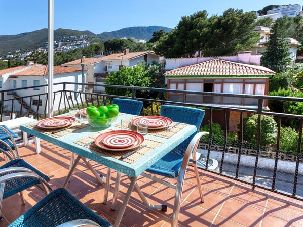 A terrace with a table set for dining, surrounded by blue chairs, and overlooking a residential area with houses and trees. - Nice apartment for 4 guests with A/C, TV and terrace (Llançà)