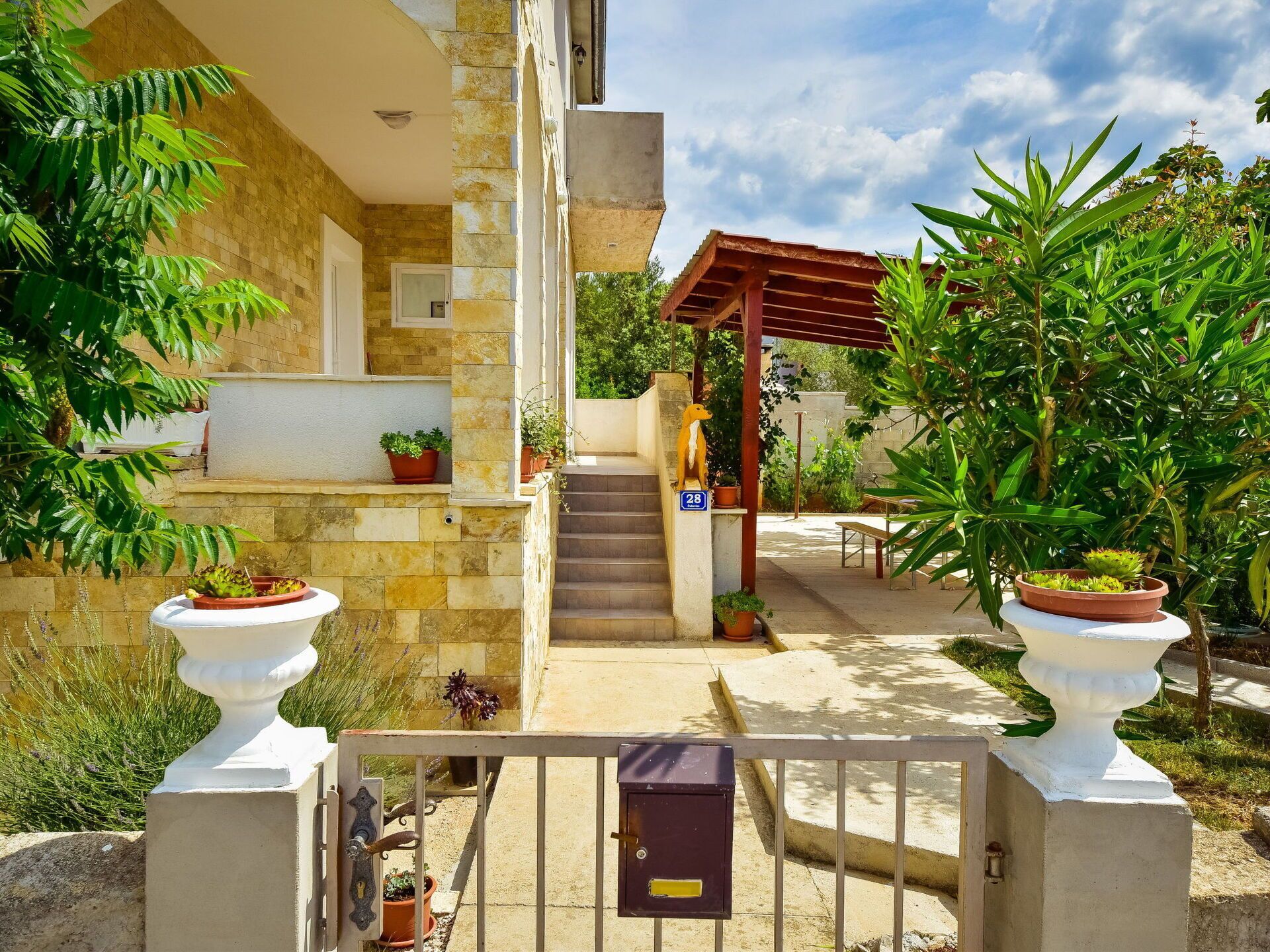 A stone building with a covered entrance, potted plants, and a metal gate.