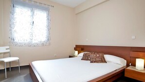 A neatly made bed with a wooden headboard, a bedside table with a lamp, a chair, and a window with patterned curtains. - Nice apartment for 4 guests with pool, A/C, TV and terrace (Calpe)
