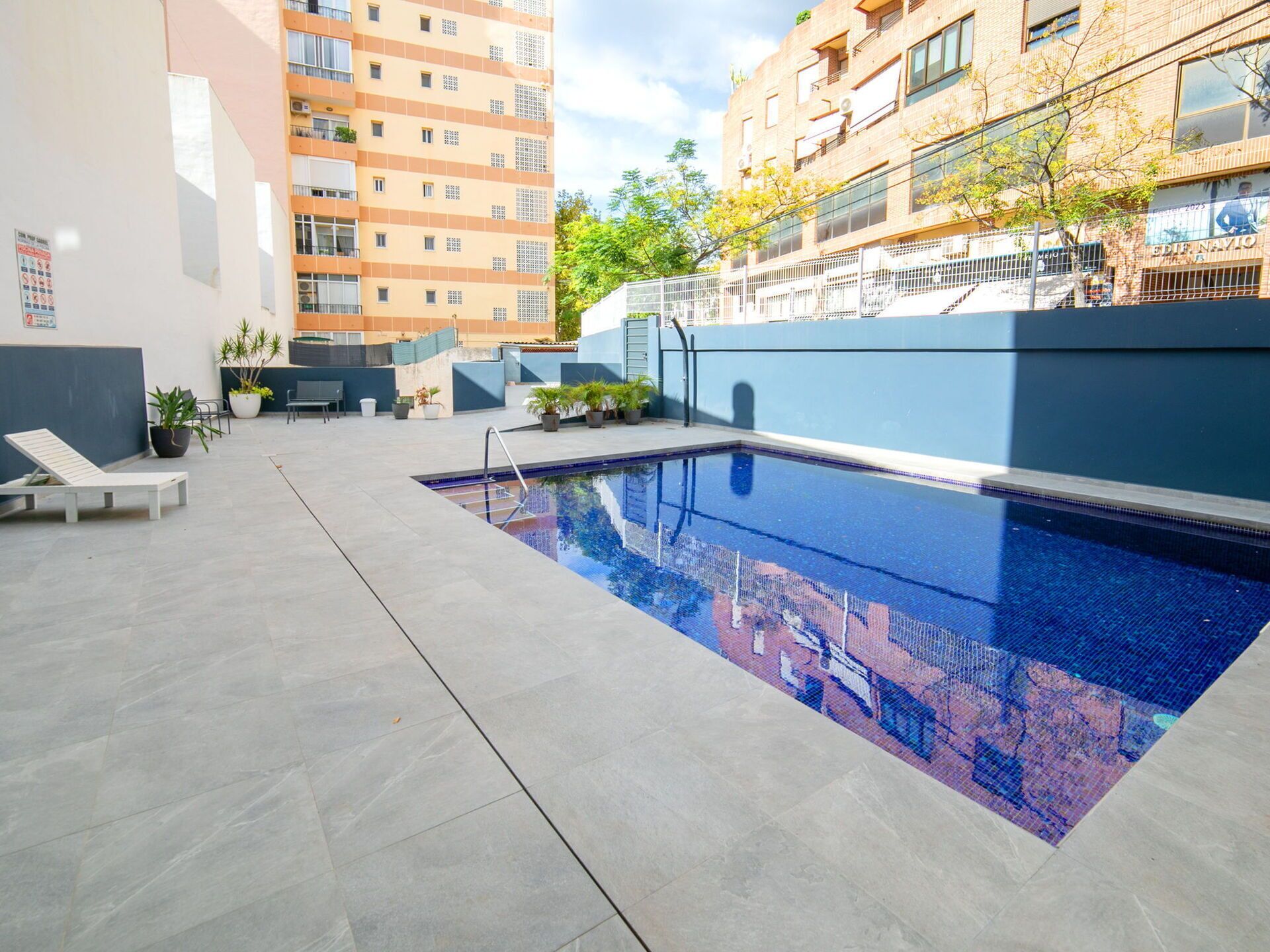 A swimming pool with a tiled deck, lounge chairs, and potted plants.