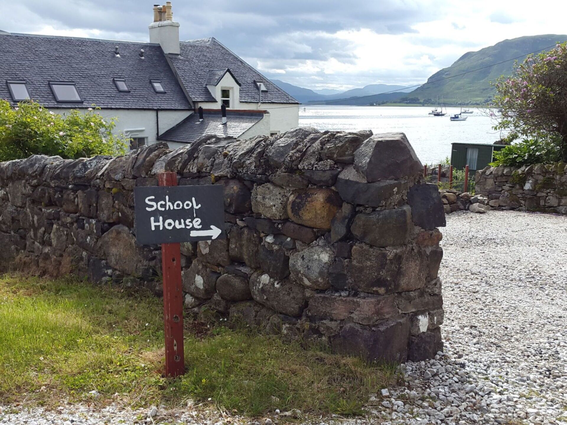 A stone wall with a sign pointing to a schoolhouse.