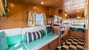 A compact RV interior with a kitchenette, a seating area with cushions, and a checkered floor. - Blue Skies Resort / Glamping / Pool / Fireplace (Willow City)