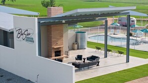 A modern building with a patio area featuring outdoor seating, a fireplace, and a pool. - Miss Abby / Glamping / Pool / Outdoor Fireplace (Willow City)