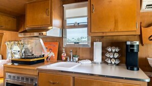 A compact kitchenette with wooden cabinets, a stainless steel range hood, a microwave, a coffee maker, and a window with a view.