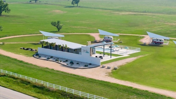 Un edificio moderno con amplio estacionamiento, mesas al aire libre y vistas al campo circundante.