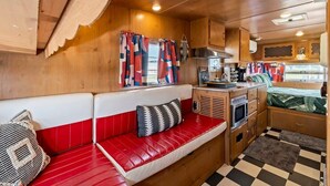 Interior compacto de una autocaravana con kitchenette, un área de descanso con un banco acolchado rojo y una ventana con cortinas coloridas.