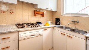 Une cuisine compacte avec des meubles blancs, une cuisinière à gaz, une machine à café et une fenêtre donnant sur une rambarde rouge.