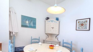 Un coin repas avec une table ronde, des chaises bleues, un meuble blanc et un luminaire suspendu.