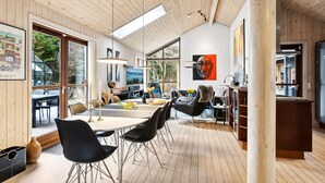 Un intérieur moderne avec un plancher en bois, un coin repas avec des chaises noires et une grande fenêtre donnant sur un espace verdoyant.