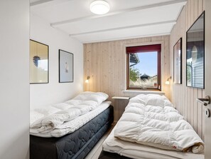 Un dormitorio con dos camas, paneles de madera en las paredes, una ventana con vistas y cuadros enmarcados.