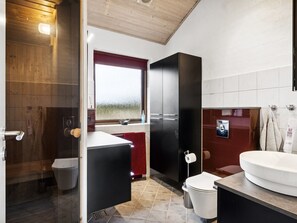 Un baño moderno con techo de madera, un ventanal grande, un mueble negro, un lavamanos blanco y un perchero rojo.