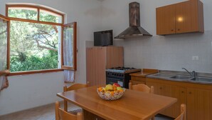 Une cuisine avec une table en bois, des chaises, une cuisinière, un évier et une fenêtre donnant sur des arbres.