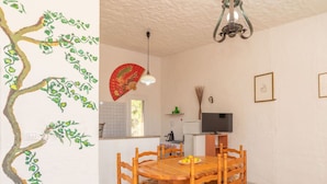 Zona pranzo con un tavolo rotondo in legno e sedie, una ventola a soffitto, una televisione e un dipinto decorativo a parete.