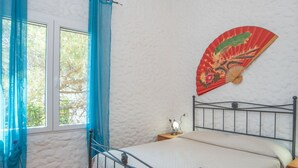 Una camera da letto con un letto, un comodino, una ventola a muro e una finestra con tende blu.