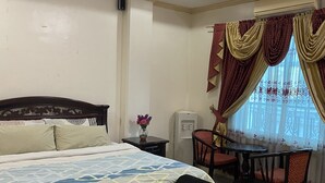 A hotel room with a bed, a small table with chairs, a ceiling fan, and a window with curtains. - Rovimar Condo Angeles  (Angeles City)