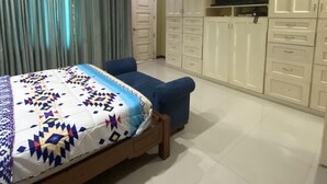 A bedroom with a bed, a blue chair, a ceiling fan, and a TV on the wall. - Rovimar Condo Angeles  (Angeles City)