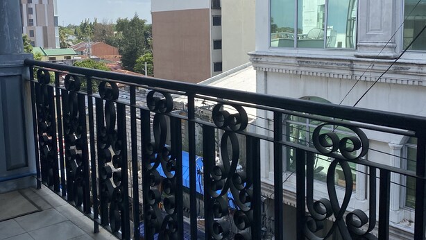 A balcony with ornate black metal railings, overlooking a cityscape with modern buildings and a clear sky. - Rovimar Condo Angeles  (Angeles City)
