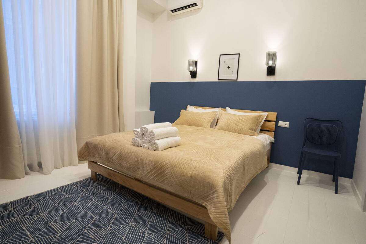 A hotel room with a bed, a chair, a wall-mounted light, and a framed certificate on the wall.