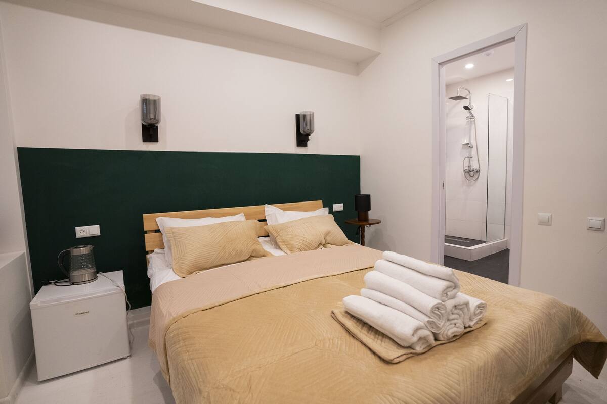 A hotel room with a bed, a nightstand, a coffee maker, and a shower area.
