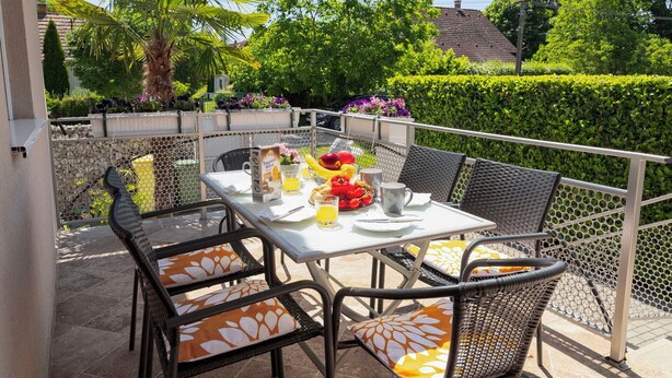 En terrasse med et bord dækket til morgenmad, udendørs stole og udsigt til haven.