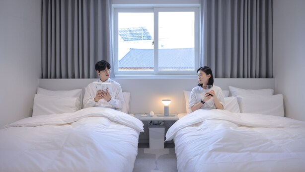Une chambre d’hôtel avec deux lits, une table de chevet avec une lampe et une fenêtre avec des rideaux.