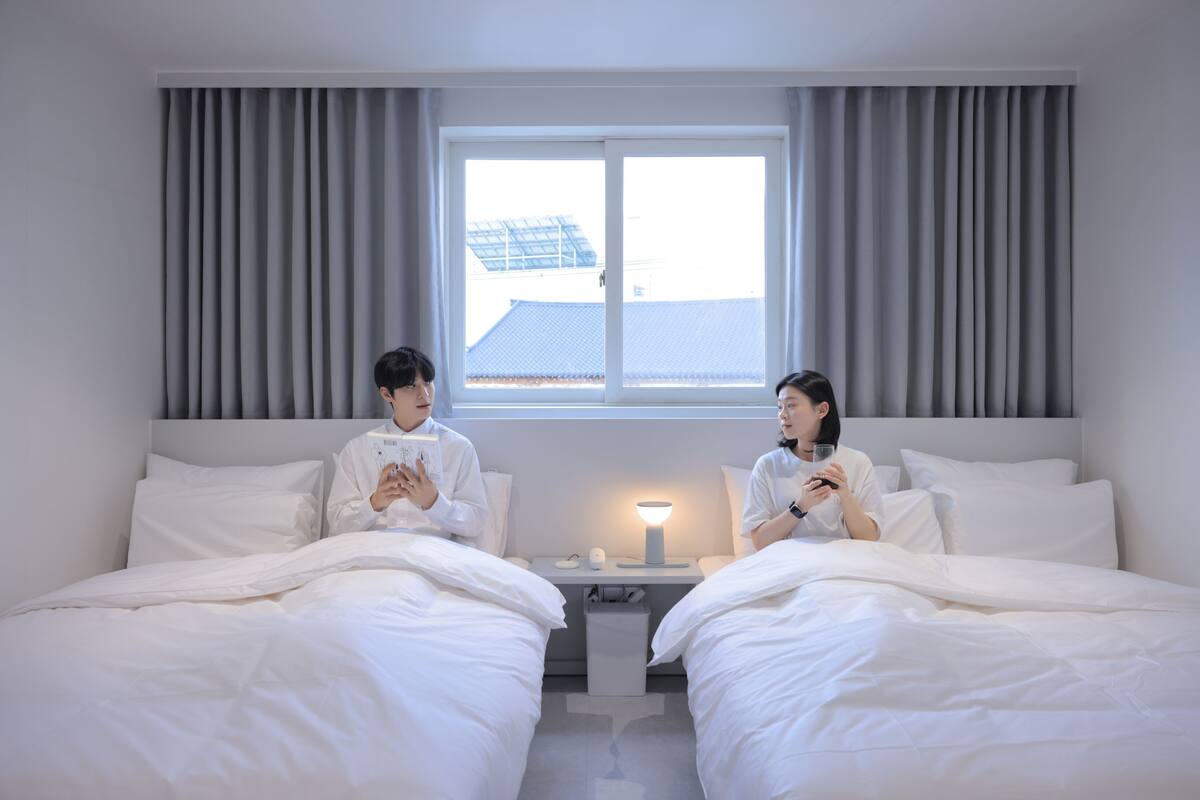 Een hotelkamer met twee bedden, een nachtkastje met lamp en een raam met gordijnen.