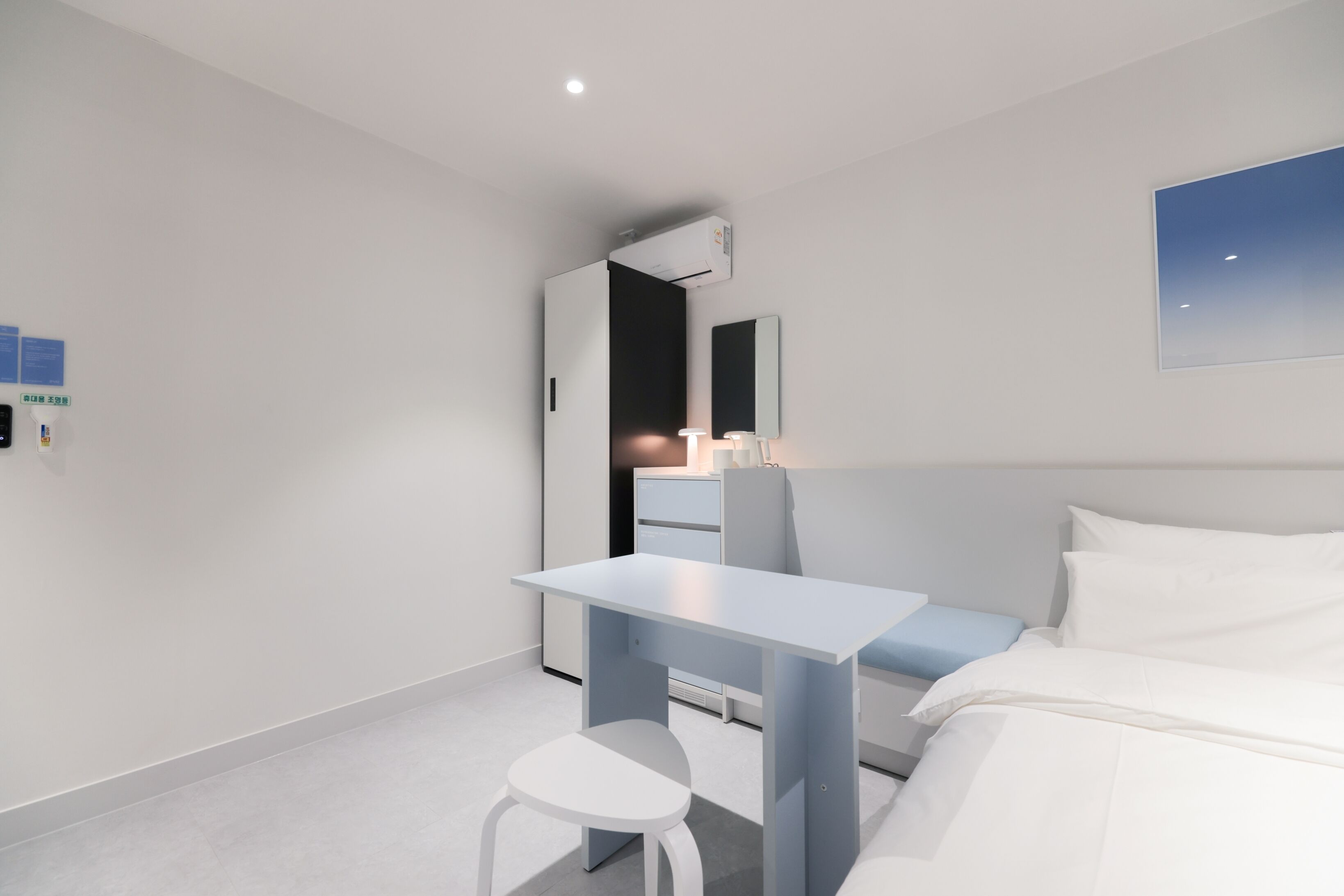 Une chambre d’hôtel moderne équipée d’un lit, d’un bureau et d’une chaise. On y trouve une table de chevet avec une lampe, ainsi qu’un climatiseur fixé au mur.