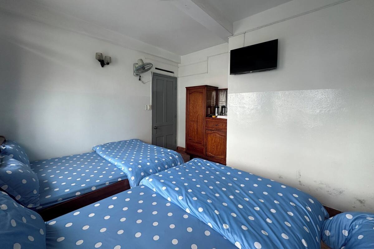 Une chambre avec deux lits, une armoire en bois, une télévision et un ventilateur de plafond.