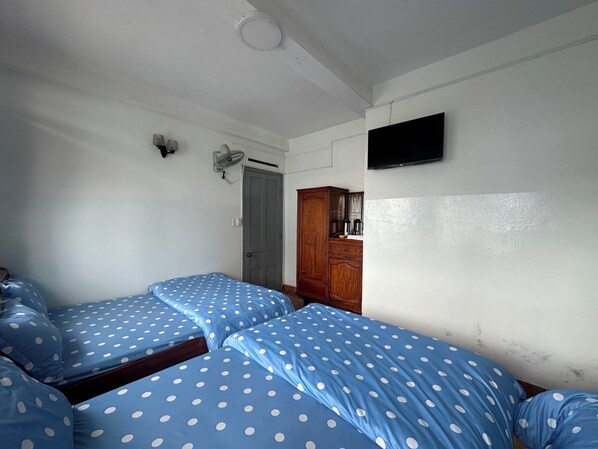 A room with two beds, a wooden wardrobe, a television, and a ceiling fan.