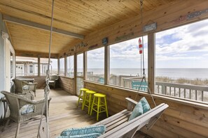 Relax in a tranquil beachside setting with a wooden deck, wicker chairs, and a hanging chair, offering stunning ocean views.