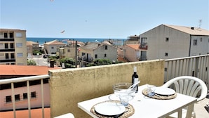 A balcony with a table set for two, overlooking a coastal town with buildings and the sea. - Nice apartment for 2 guests with WIFI, TV, balcony and pets allowed (Narbonne)