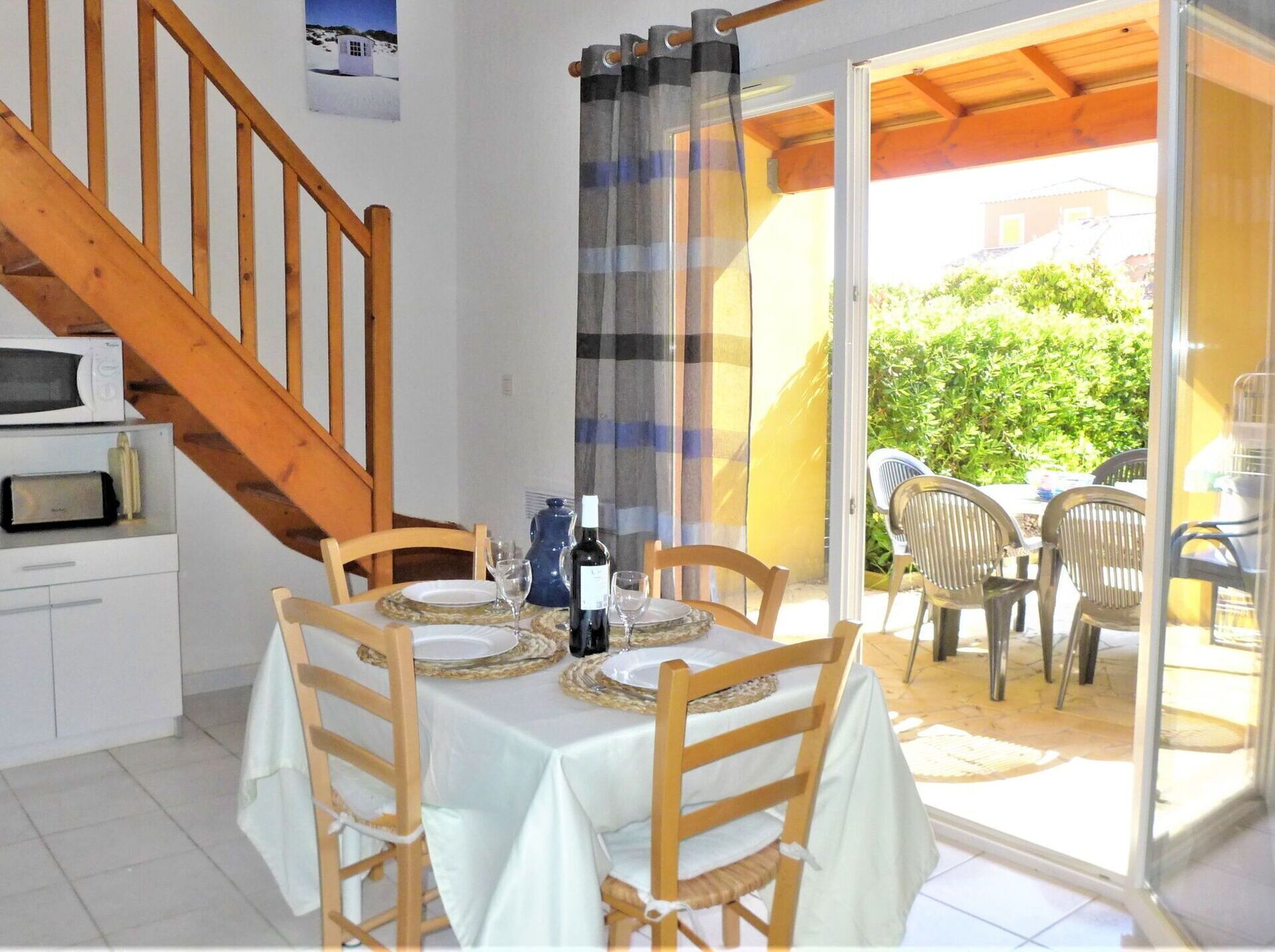 Un comedor con una mesa dispuesta para dos, una escalera de madera y vistas al exterior.