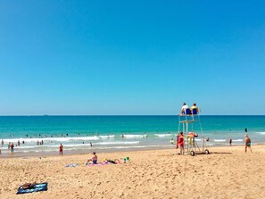 Ein Strand mit Rettungsschwimmern in einem Turm, badenden Personen und einem sandigen Ufer.