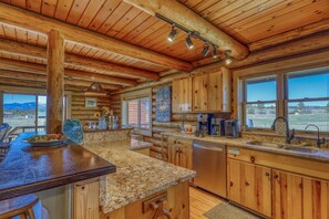Une cuisine rustique dans un chalet, avec des meubles en bois, des comptoirs en granit et une grande fenêtre offrant une vue sur les montagnes.