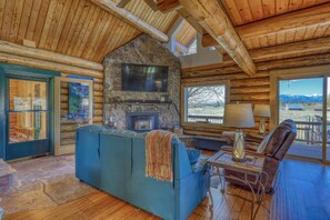 L’intérieur d’une cabane en rondins, avec une cheminée en pierre, un grand canapé bleu et une vue sur les montagnes.