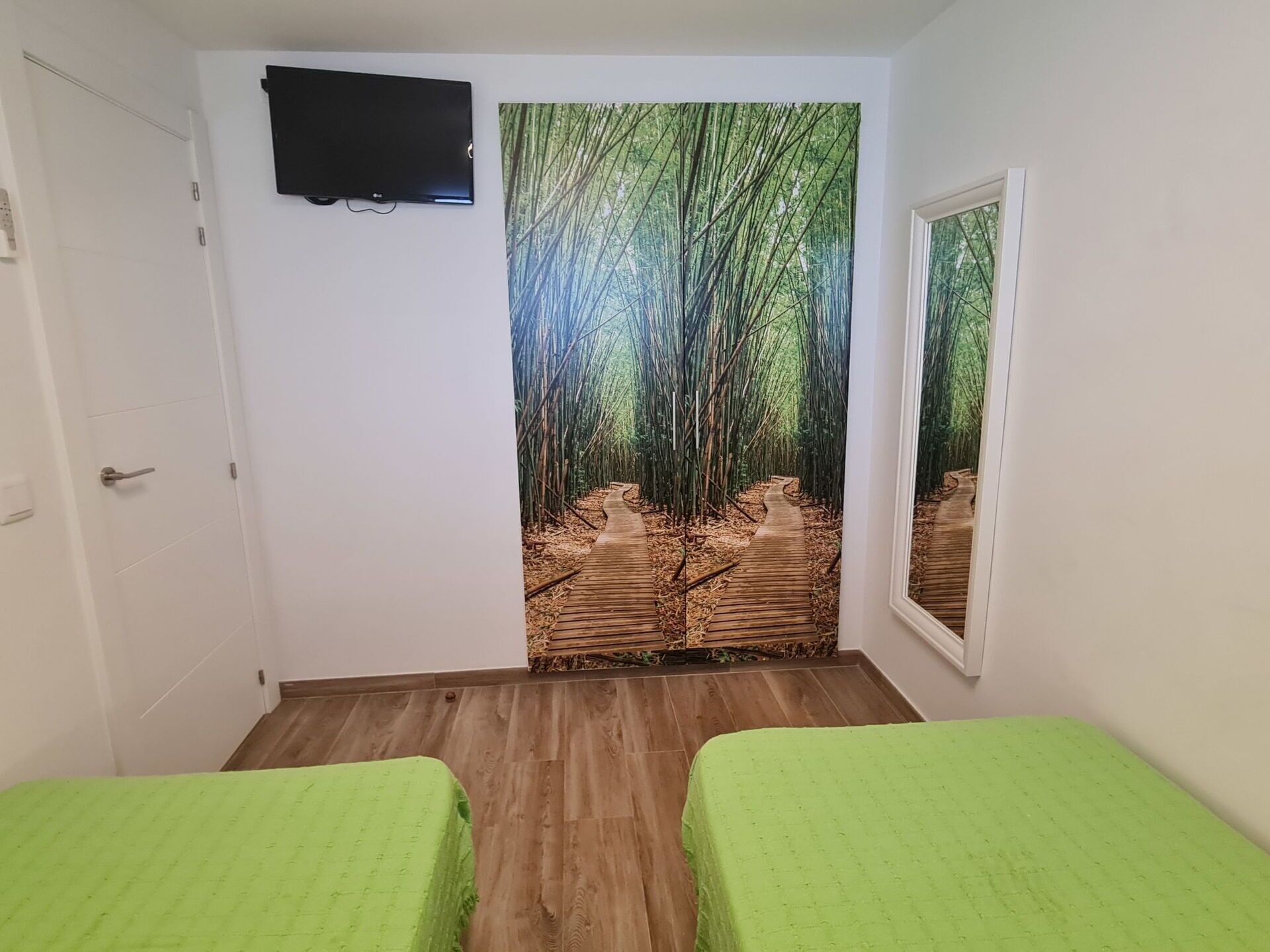 A room with two beds, a wall-mounted TV, and a large bamboo forest mural.