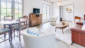 Ein geräumiges Wohnzimmer mit Essbereich, einem weißen Sofa, einem braunen Ledersessel und einem Holzschrank mit Fernseher.