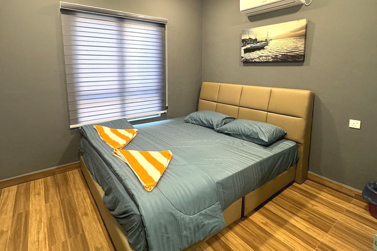 A bedroom with a bed, a window with blinds, a wall-mounted air conditioner, and a picture of a boat on the wall.