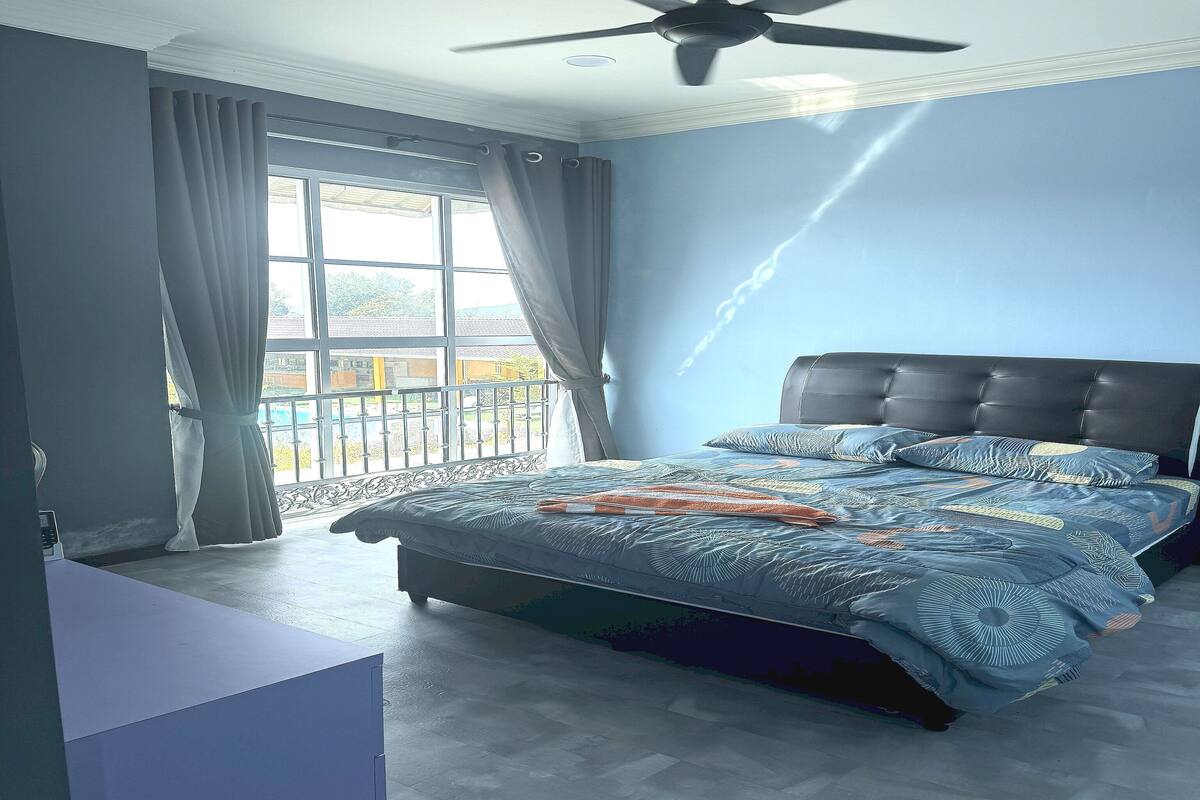 A bedroom with a bed, a ceiling fan, a window with curtains, and a view of the outside.